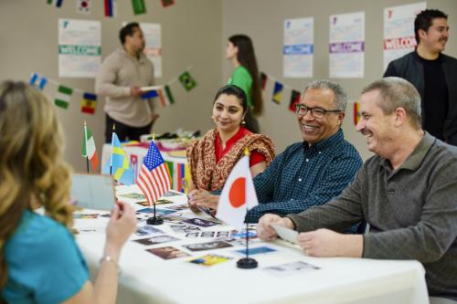 Various people sit at a table with multiple countries' flags displayed. 