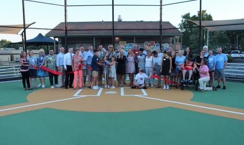 A large group of people stand near home plate, posed for a photo, during a ribbon cutting of the Mark Teahen Family Field