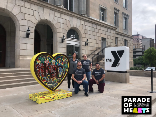 Four Y employees pose next to "Garments of Rabbitville" by Jacob Luke, a heart created for the Parade of Hearts event in 2024, located outside of the Kirk Family YMCA.