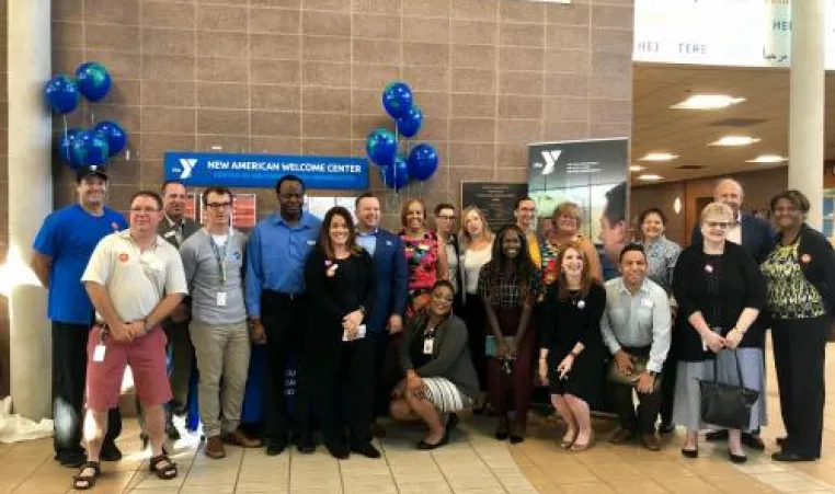 Event attendees and Y staff gather for a photo in front of the New American Welcome Center.