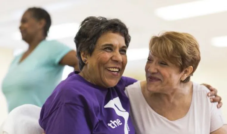 Two happy older women leaning into each other while sitting down 