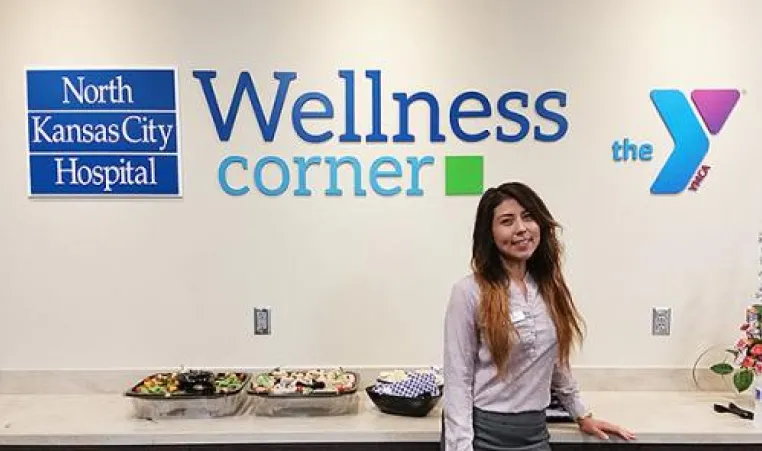 Young woman stands in front of the NKCH Wellness Corner sign at the North Kansas City Hospital 