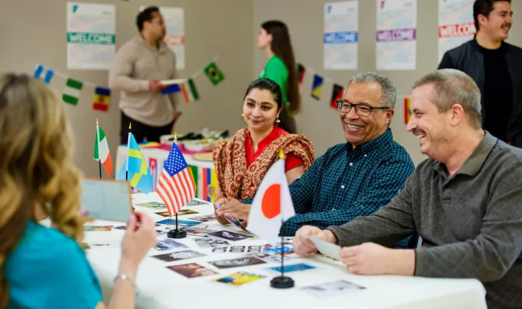 People of multiple nationality sit across from each other at a table covered in multiple countries' flags at a Kansas City YMCA.