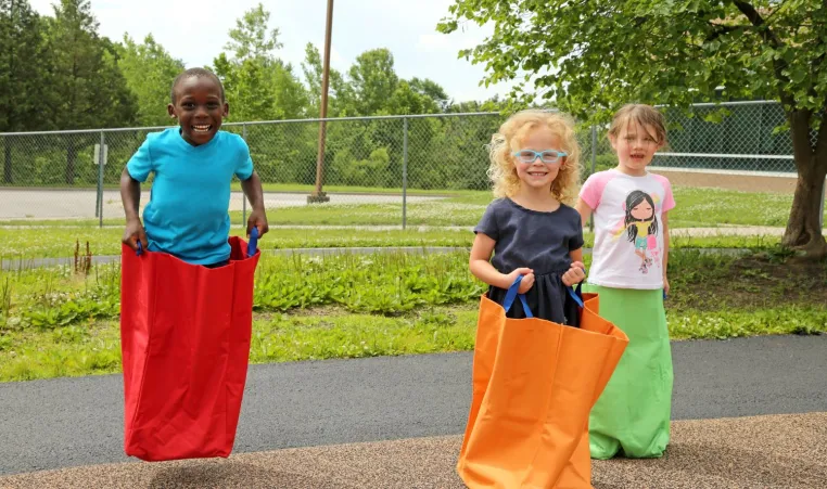 3 Children in the Head Start program jumping in jumping bags on the Kansas City YMCA playground.