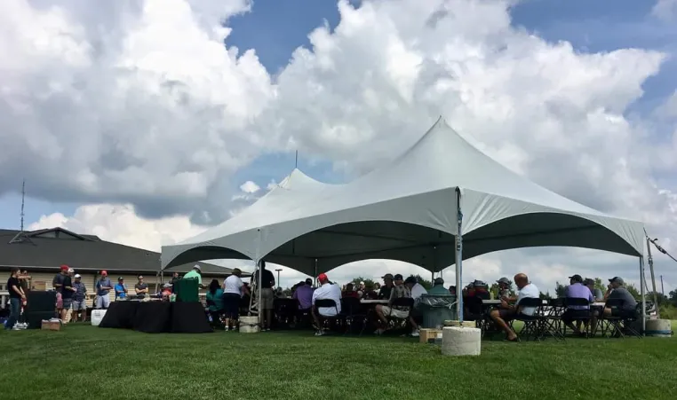 Large white tent with open sides shield golfers, seated at tables, from the sun at the Olathe Golf Tournament