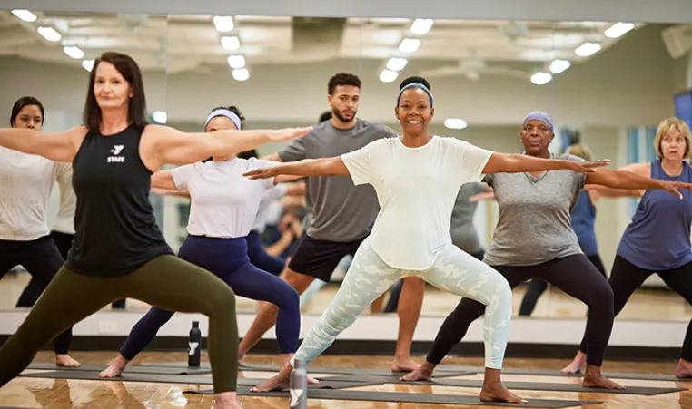 A group of YMCA members in the warrior 2 pose practicing yoga in a Kansas City YMCA group class.