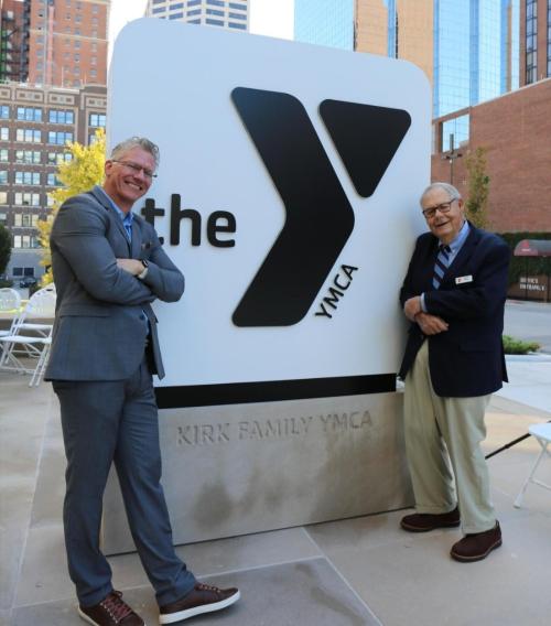 CEO Mark Hulet and longtime Y supporter Frank Kirk pose next to the large Y logo monument sign outside of the Kirk Y at the ribbon cutting of that event on October 14, 2021