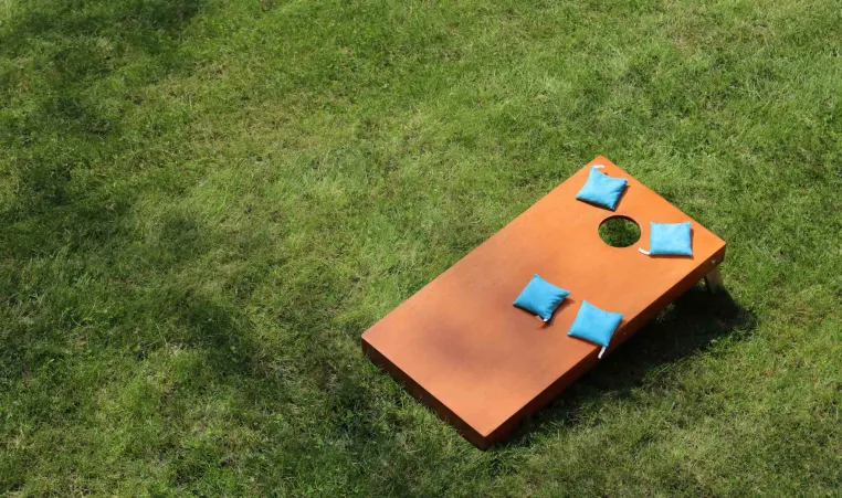 A wooden cornhole board sitting on the grass with 4 blue bags on the board.