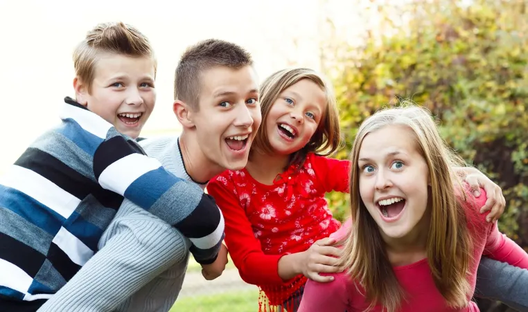 two babysitters outside giving a piggy back ride to the two kids they are watching.