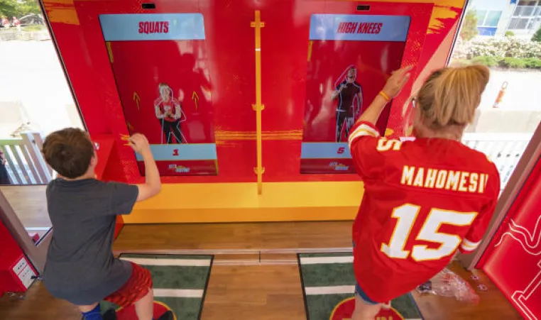 Woman in Mahomes Kansas City Chief's jersey and child working out in front of Chiefs Training Lab Powered by GEHA.