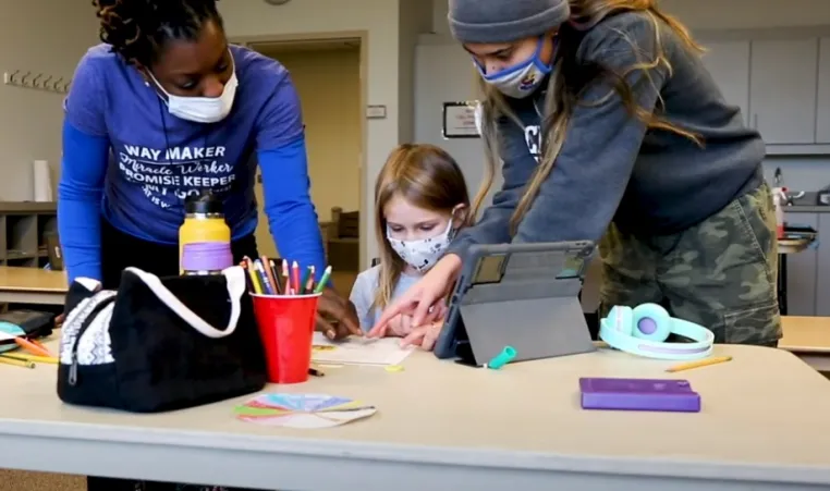 2 YMCA team members instructing a student on homework at a desk.