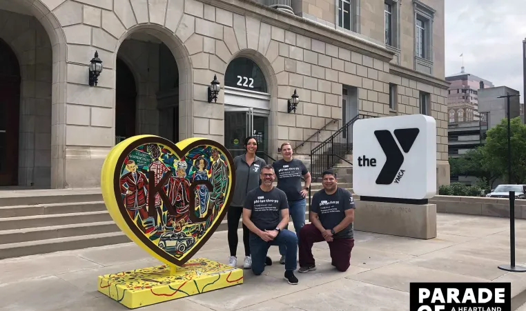 Four Y employees pose next to "Garments of Rabbitville" by Jacob Luke, a heart created for the Parade of Hearts event in 2024, located outside of the Kirk Family YMCA.