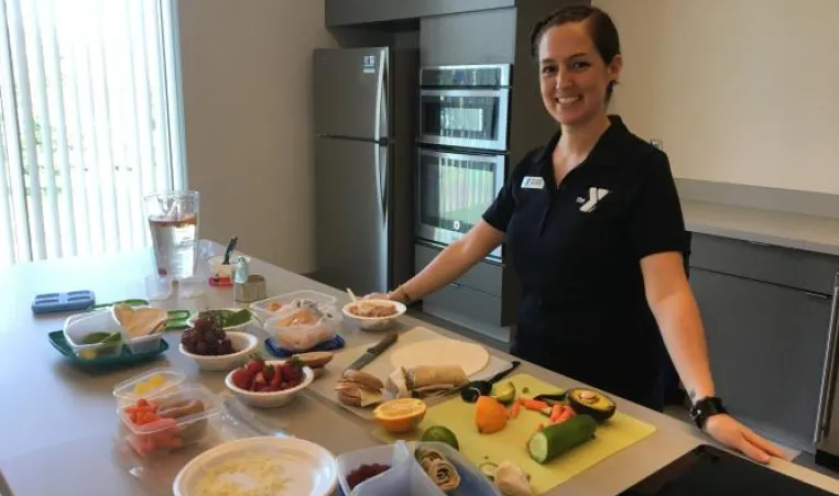 Greater Kansas City YMCA team member standing in front of a food prep table where fresh fruit and vegetables are being prepped.