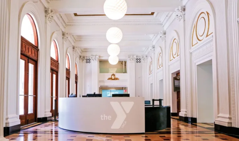 Photo of the lobby of the new Kirk Family YMCA. Shows restored lobby of the historic Lyric Theatre. In the center is the white welcome center desk with a Y logo on it.