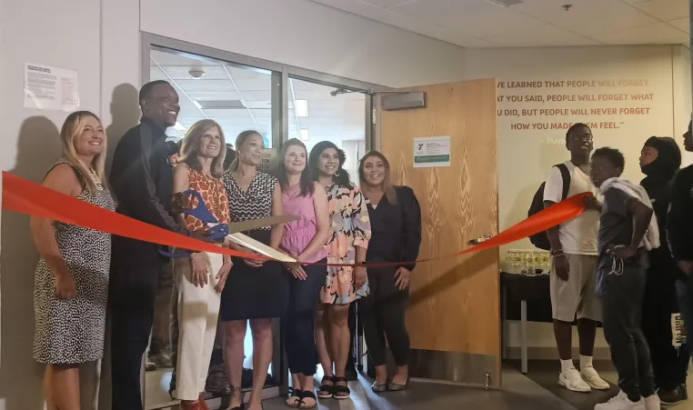 Staff and volunteers hold large ribbon and scissors in front of new teen tech center space at Linwood YMCA.