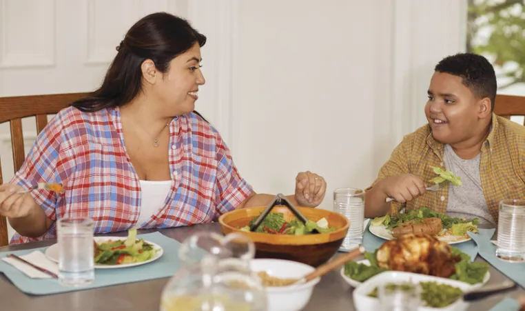 Mother and son sit at dinner table smiling as they eat a healthy meal.