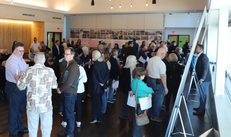 Photo of Prairie Village Community Center Campus Study public meeting on April 4, 2024. Guests look at boards with potential site configuration plans and talk with other guests and representatives from partners.