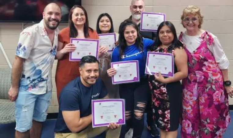 A group of eight ESL students pose for a photo with their completion certificates in a recent graduation ceremony