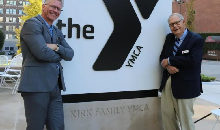 Photo of Mark Hulet and Frank Kirk in front of the Kirk Family YMCA sign.