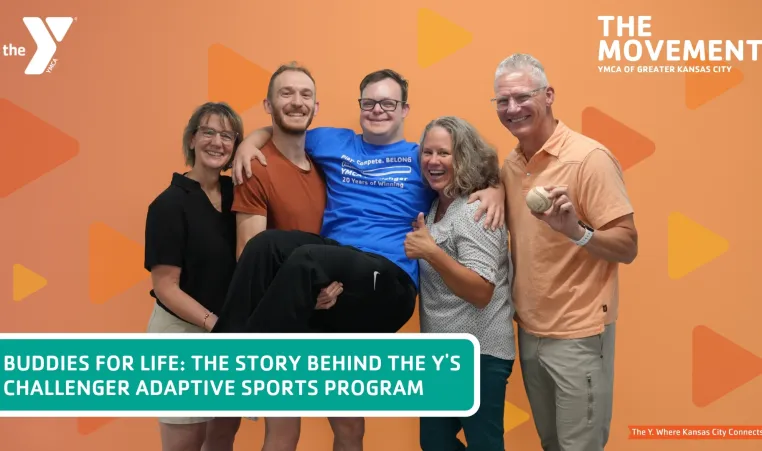 Five people huddle together to pose, while 2 people hold up the gentleman in the middle, everyone is smiling