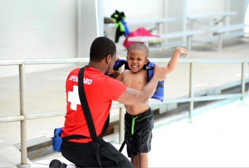 Photo of a lifeguard helping a young boy put on a life jacket