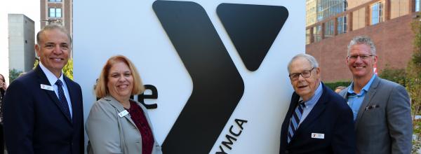 President and CEO John Mikos; Chief Financial Officer Kelli McClure; Board member and donor Frank Kirk; Chief Operating Officer Mark Hulet stand together by the large Y logo monument sign in front of the Kirk Family YMCA