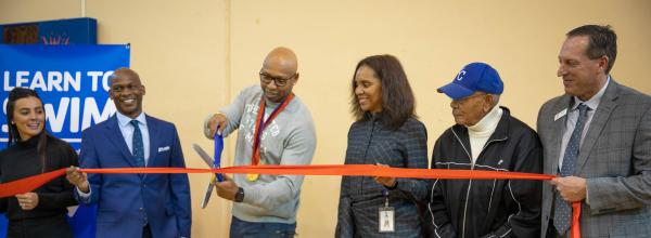 Partners stand for ribbon cutting. Olympian Cullen Jones holds scissors