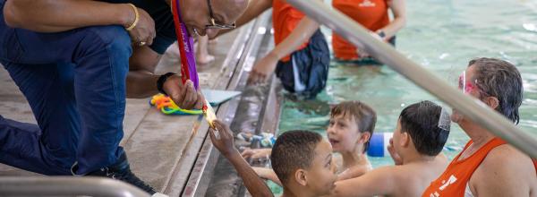Cullen Jones leans over edge of pool to show students and swim instructor his Olympic medals.
