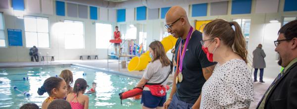 Cullen Jones, wearing Olympic medals, talks to students and staff on pool deck 